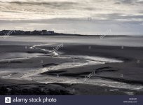 a-stream-meanders-through-mudflats-at-low-tide-in-morecambe-bay-with-the-seafront-of-sandyland...jpg